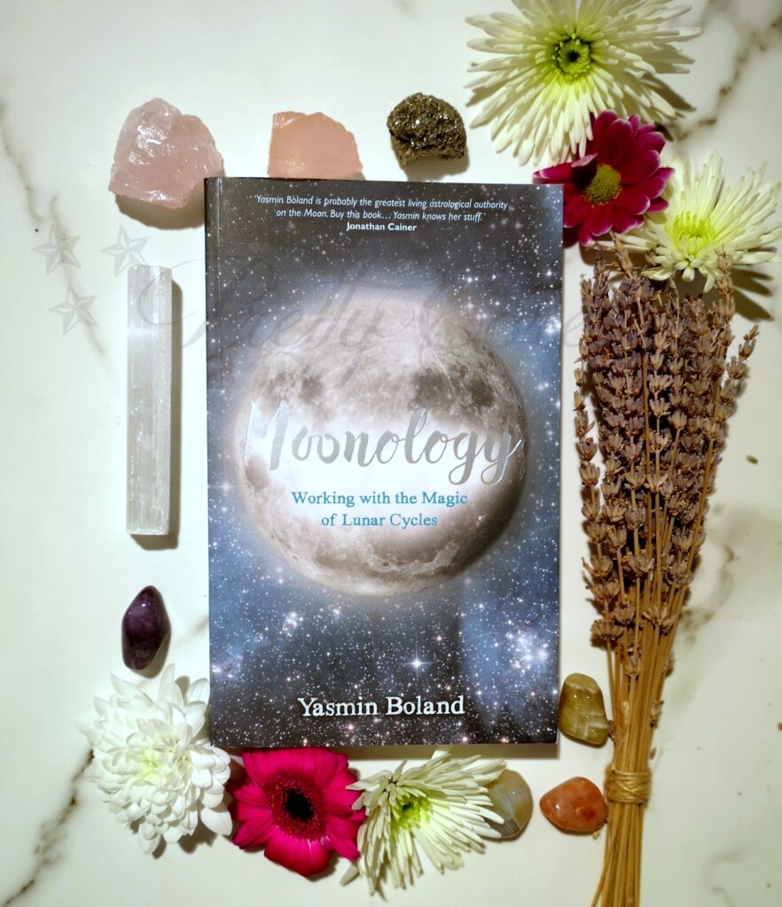 Moonology Book Yasmin Boland With Flowers and Crystals surrounding the book