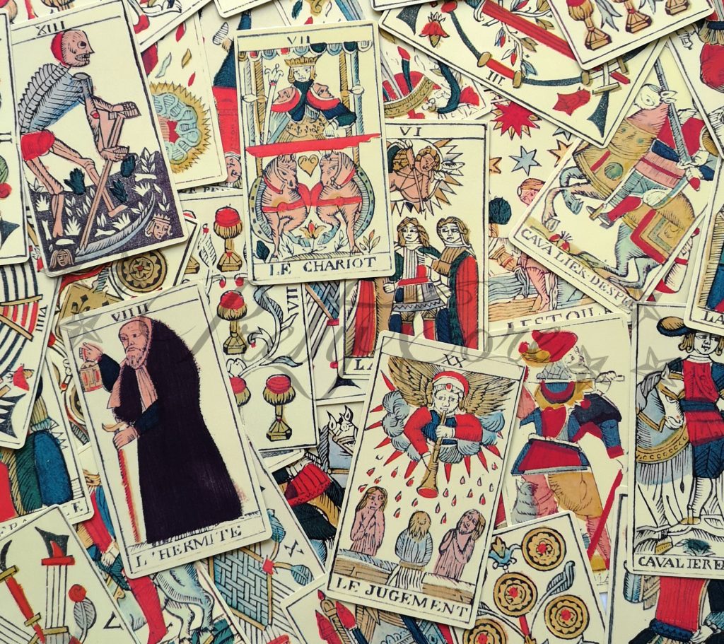 Tarot De Marseille bunched together and showing the range of cards, from major to minor arcana, cream with primary colours
