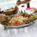 Hands around a vegan salad serving other people