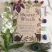 The House Witch Book by Arin Murphy-Hiscock surrounded by slwoers, crystals and a peacock feather.