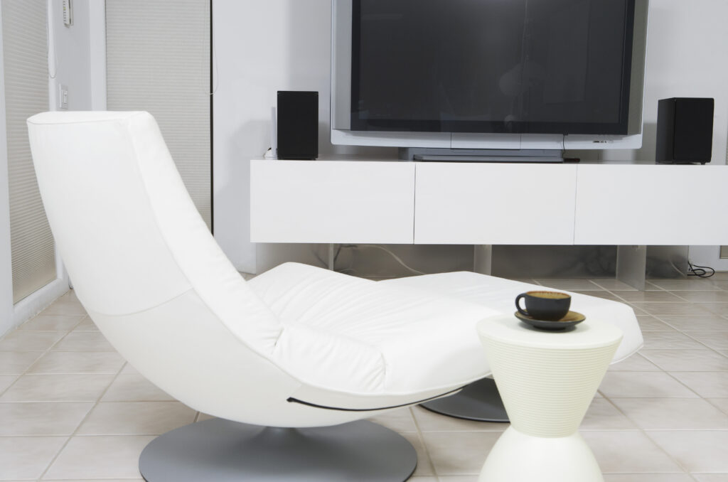 Reclining chair infront of a TV with speakers and a round console table with a coffee cup on there