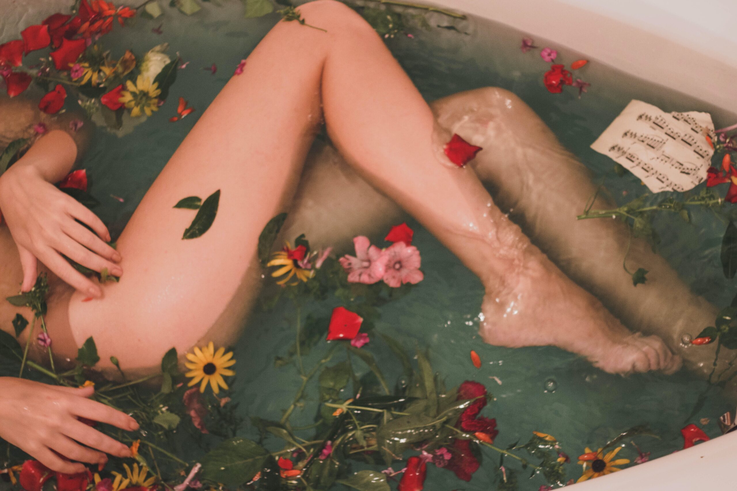 Bath filled with flowers and petals and showing a pair of naked legs and skin silky soft