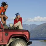 Red SUV with a man sat on the roof and woman sat on the bonnet