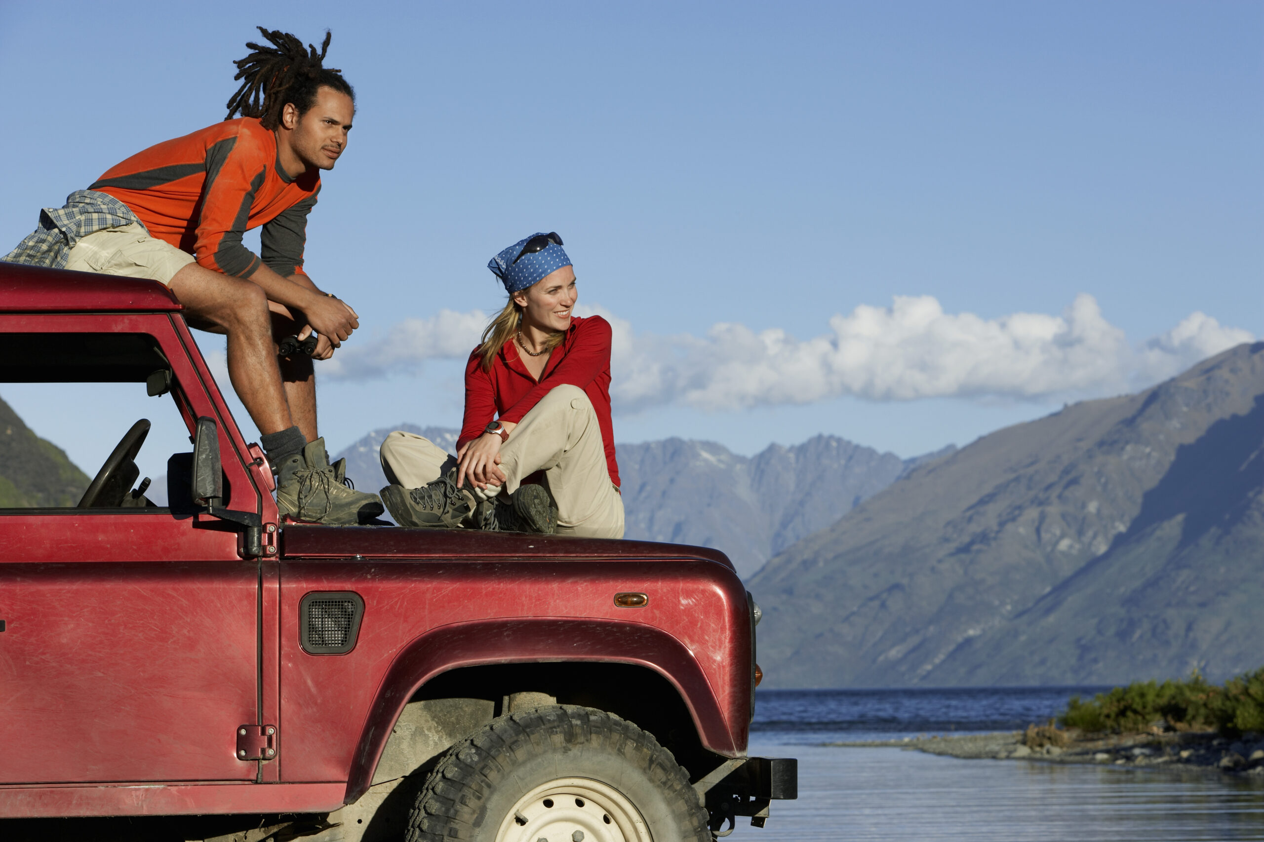 Red SUV with a man sat on the roof and woman sat on the bonnet