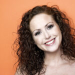 Woman with an orange background smiling as Issues Will Age You Before Your Time