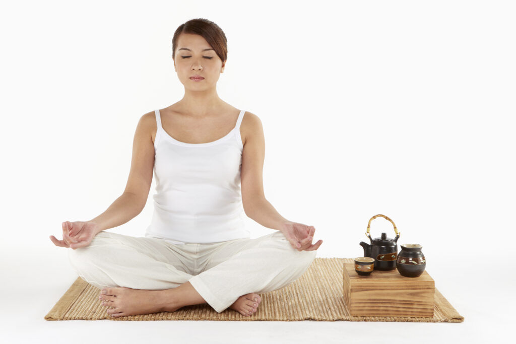 Woman sitting and meditating wearing white with a tea set next to her