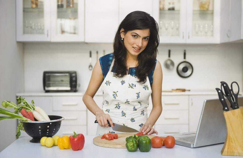 Woman stood in the kitchen chopping vegetables with a laptop next to her Cut Costs By Online Dating - Top 4 Tips For Budget Dating