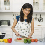 Woman stood in the kitchen chopping vegetables with a laptop next to her Cut Costs By Online Dating - Top 4 Tips For Budget Dating