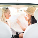 2 women in the front of a car holding up a map on a road trip